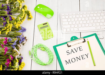 Arbeitsplatz mit Wireless slim Tastatur, grüne Maus, Zwischenablage mit den Worten AVE GELD', Taschenrechner, Bleistift, Netzkabel, bunte Blumen auf Weiß nicht Stockfoto