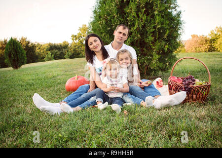 Schöne freundliche Familie mit zwei Kindern auf einem Picknick im Park. Vater umarmt seine Frau und zwei Töchter Stockfoto