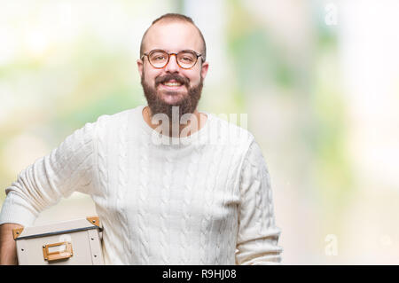 Junge hipster Mann mit Brille, beweglichen Holding Kasten über isolierte Hintergrund mit einem glücklichen Gesicht stehen und lächelnd mit einem selbstbewussten Lächeln sh Stockfoto