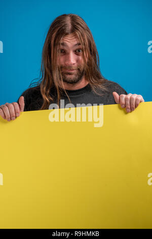 Portrait von langhaarigen Mann, der ein lustiges Gesicht, während sie einen Blauen werben Banner. Copyspace für Nachrichten oder Informationen verfügbar Stockfoto