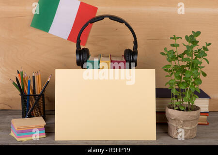 Konzept für das Erlernen der italienischen Sprache - leeres Papier, Flagge der Italia, Bücher, Kopfhörer, Bleistifte auf hölzernen Hintergrund Stockfoto