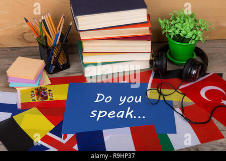 Sprachen lernen Konzept - Papier mit Text 'Do sprechen Sie...', Flaggen, Bücher, Kopfhörer, Bleistifte auf hölzernen Hintergrund Stockfoto