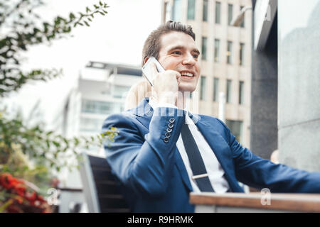 Junge attraktive Geschäftsmann Gespräch per Handy in Street Cafe, lächelnd und gerade auf der Suche. Stockfoto