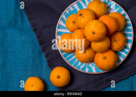 Drei reife lecker saftig Mandarin liegen in einem hellen Weiß mit einem blauen Platte Muster auf dem Stoff Tuch, Handtuch für die Küche Stockfoto