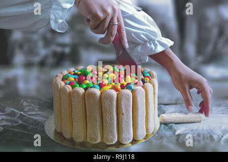 Weibliche Hände einen Kuchen mit viel Farbe rund Pralinen bei einem Kinderfest. Stockfoto