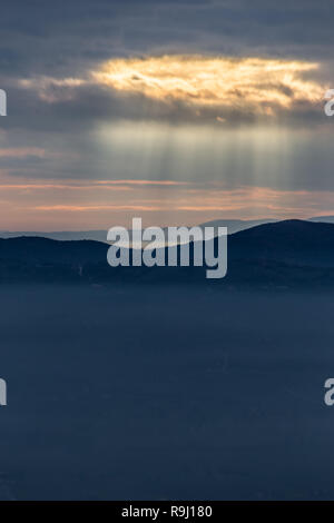 Sonnenstrahl scheint durch Wolken über die Berge und ein Meer von Nebel Stockfoto