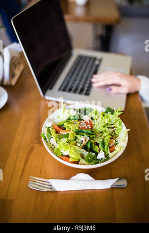 Junge Frau sitzt mit Laptop in ein Cafe und Essen heathty Salat auf den Tisch. Stockfoto