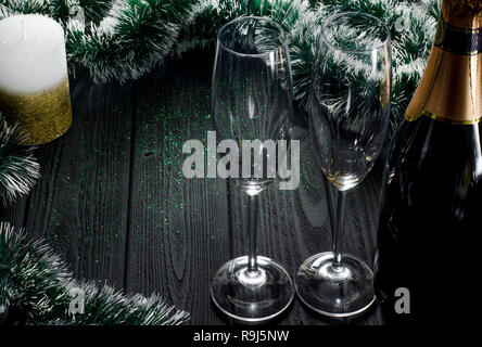 Eine Flasche Champagner und zwei Gläser stehen auf einem dunklen Grau Holztisch von Weihnachtsschmuck und einer weiß-gold Kerze steht neben es umgeben. Stockfoto
