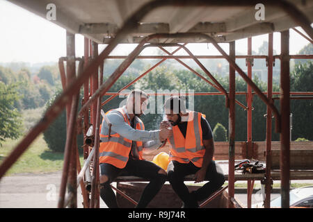 Zwei glückliche Männer lachen bei der Arbeit in der Baustelle. Team der Arbeitnehmer rauchen Zigarette und Sprechen während der Pause Stockfoto