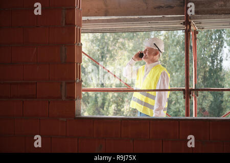 Menschen, die in Baustelle. Mann bei der Arbeit im neuen Haus im Haus. Foreman Wandern auf Gerüsten und im Gespräch mit Handy Stockfoto