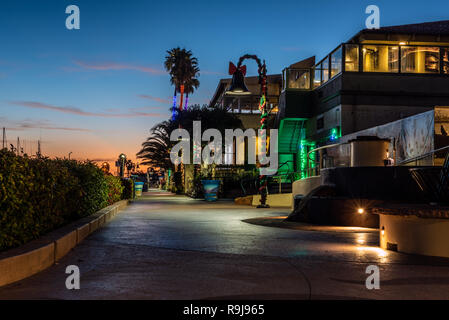 Weihnachtsbeleuchtung aufgewickelt um die Lampen und Palmen unter Dämmerung Himmel entlang Ventura Harbour Shops in Kalifornien, USA, am 24. Dezember 2018. Stockfoto