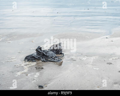 Kunststoff schwarz Müllbeutel gewaschen oben auf Ufer- und umweltschädliche Shoreline. Metapher Kunststoff Verschmutzung, Umweltverschmutzung, Krieg auf Kunststoff, plastik Müll Stockfoto