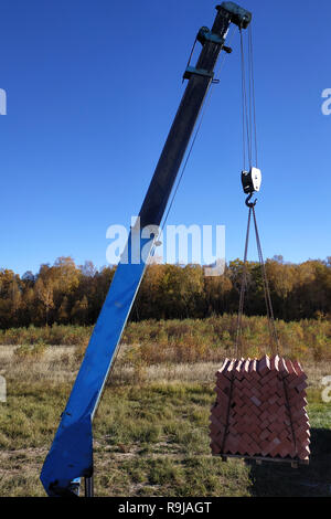 Das Auto Kran hält und entlädt die Ziegel auf dem Hintergrund der blauen Herbsthimmel 2018 Stockfoto