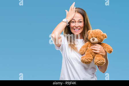 Mittleres Alter spanischer Frau mit niedlichen Teddybär Plüsch über isolierte Hintergrund mit Hand betonte am Kopf, mit Scham und Überraschung Gesicht, ang schockiert Stockfoto