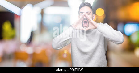 Jungen gutaussehenden Mann mit Sweatshirt über isolierte Hintergrund schrie wütend, laut mit den Händen über Mund Stockfoto