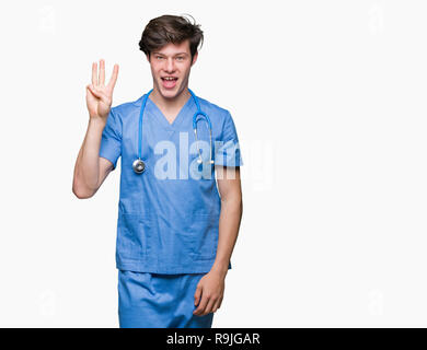 Junger Arzt mit medizinischen gleichmäßig über isolierte Hintergrund angezeigt und zeigen mit den Fingern Nummer drei, während lächelte zuversichtlich und fröhlich. Stockfoto