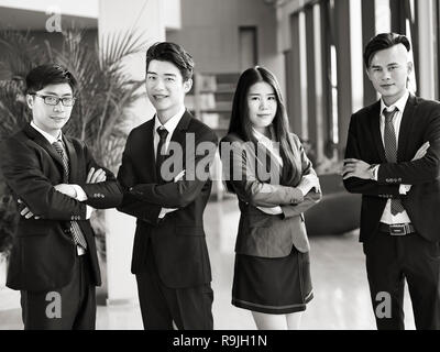 Porträt einer Gruppe von jungen asiatischen Geschäft Leute im Amt stehende Arme gekreuzt, in die Kamera lächeln, Schwarz und Weiß. Stockfoto