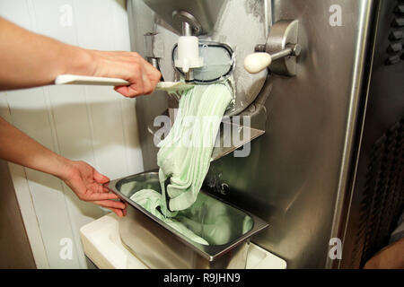 Weibliche Konditor in Chef einheitliche arbeitet an ice cream maker Maschine. Die Minze Eissorten und es fällt in Stahl container. Stockfoto