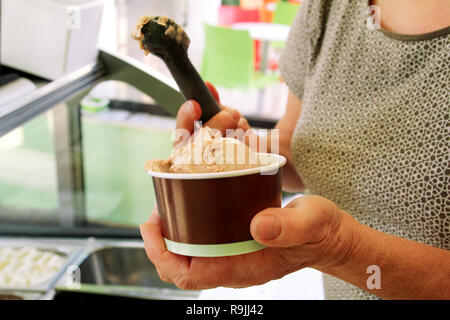 Weibliche hand mit Schaufel nimmt Eis aus dem Kühlschrank und in Karton Eisbecher serviert. Frau, die Kugel leckeres Eis. Stockfoto