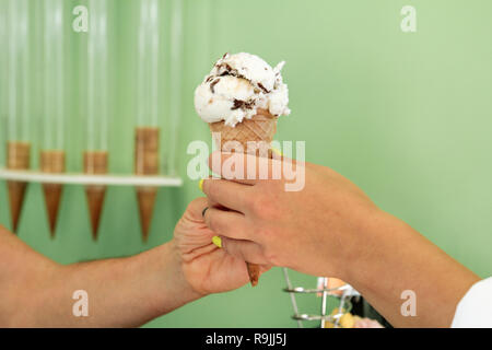 Zwei weibliche Hände halten Ein mit Schokolade Vanille Eis. Frau verkauft Eis in Konditorei und halten Eis in der Waffel Kegel. Stockfoto