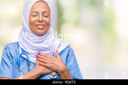 Mittleres Alter älteren arabischen Krankenschwester Frau, tragen, Hijab über isolierte Hintergrund lächelnd mit der Hand auf der Brust mit geschlossenen Augen und dankbare Geste auf das Gesicht. Uhr Stockfoto