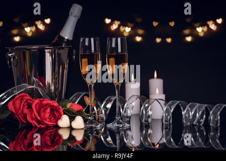 Flasche Champagner im Eimer mit zwei Weingläser, Blumenstrauß aus Rosen, Pralinen und Kerzen in Herzform mit Licht auf schwarzem Hintergrund. Liebe, Vale Stockfoto