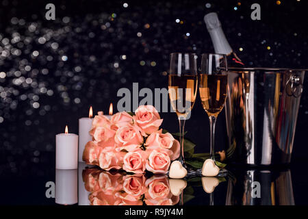 Flasche Champagner im Eimer mit zwei Weingläser, Blumenstrauß aus Rosen, herzförmige Pralinen und Kerzen auf schwarzen Hintergrund. Liebe, Valentines Tag c Stockfoto