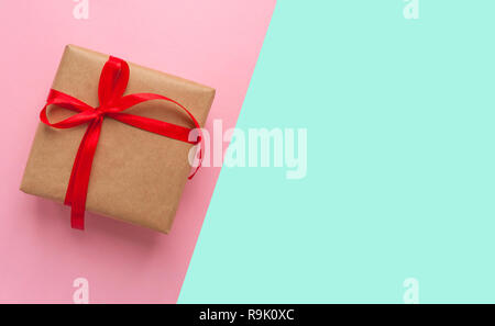 Geschenkbox in braun gefärbte Handwerk Papier gewickelt und mit roter Schleife auf Rosa und blauen Hintergrund mit Copyspace gebunden. Stockfoto