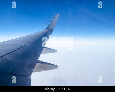 Blick auf flugzeugflügel und halo Phänomene in den blauen Himmel über bewölkt Oberfläche während des Fluges durch Bullauge Stockfoto
