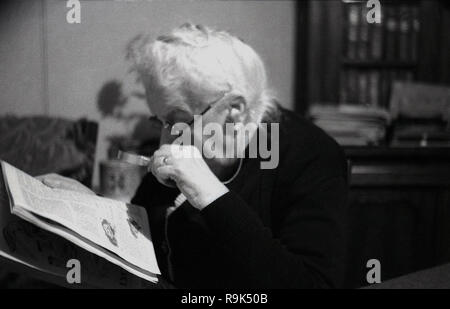 1950er Jahre, ältere Dame in einem Zimmer vorne mit einem Handheld Lupe die Drucken bis zu schließen Auf ein Magazin, England, UK lesen Sie sitzen. Die Objektiv montiert in einem Frame hilft Vergrößern Vergrößern oder Drucken in einer Zeitung oder einer Veröffentlichung dabei helfen denen mit schlechten oder fehlerhaften Sehvermögen. Stockfoto