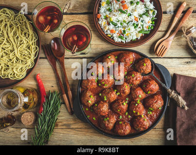 Hausgemachte Frikadellen in Tomatensoße. Pfanne auf einer hölzernen Oberfläche, Reis mit Gemüse, Pasta Stockfoto