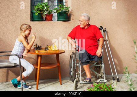 Behinderte Senior und seine schöne junge Enkelin spielt Schach und lächelnd außerhalb Stockfoto