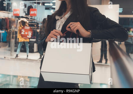 Erntegut Schuß von brunette Mädchen holding Weißbuch Einkaufstaschen am Mall Hintergrund. In der Nähe von Frau Hände halten von Paketen mit Käufen bei Verkauf Stockfoto