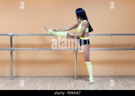 Seitliche Sicht auf eine süße Brünette Tänzerin stretching auf choreografische Maschine vor dem Hintergrund der Tanzklasse. Athletische Frau in Sportkleidung praktische Stockfoto