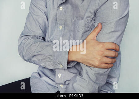 Ein Mann in einem Hemd an der Schulter, Arm, Handgelenk, Unterarm, Sport Verletzungen, Schmerzen, auf blauem Hintergrund. BRACHIUM. junger Mann hält die Stockfoto