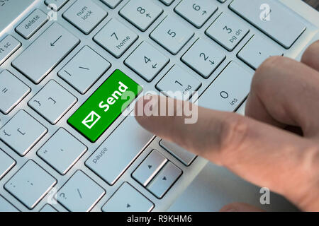 E-Taste auf der Tastatur des Computers senden, einen männlichen Finger drückt eine Taste Farbe Grau Silber Tastatur eines modernen Laptop. Taste mit der Aufschrift Stockfoto