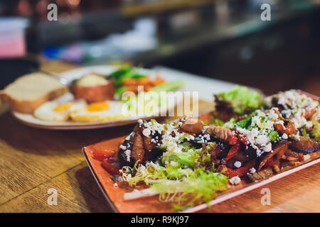 Gegrilltes Fleisch und Gemüse Rippen, Schwein, Rind, Kartoffeln, Zucchini, Auberginen, Tomaten auf einem schwarzen Brett auf dem Tisch durch Gewürze im Glas dekoriert, Schnitt Stockfoto