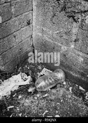 Leere PTFE-Kunststoff Trinkflasche in städtischen Backstreet verworfen. Metapher Kunststoff Umweltverschmutzung, Krieg auf Kunststoffabfälle. Schwarzweiß-Version von R 9 KJNY. Stockfoto