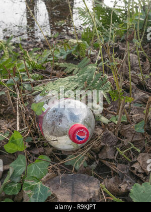 Leere PTFE-Kunststoff Soft drink Flasche in ländlichen Hecke graben verworfen. Metapher Kunststoff Verschmutzung, Umweltverschmutzung, Krieg auf Kunststoffabfälle. Stockfoto