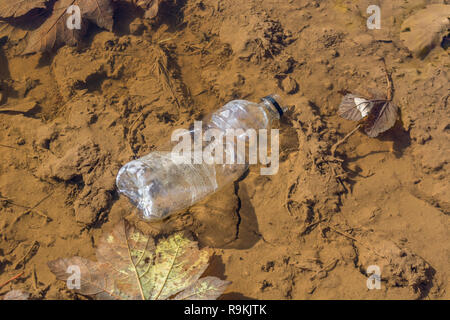 PTFE-Kunststoff Soft drink Flasche in schlammigen ländlichen Anschluss verworfen. Metapher Kunststoff Verschmutzung, Umweltverschmutzung, Krieg auf Kunststoffabfälle. Stockfoto