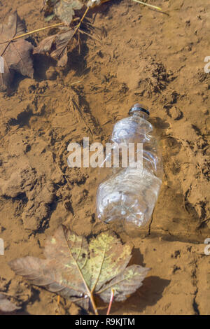 PTFE-Kunststoff Soft drink Flasche in schlammigen ländlichen Anschluss verworfen. Metapher Kunststoff Verschmutzung, Umweltverschmutzung, Krieg auf Kunststoffabfälle. Stockfoto