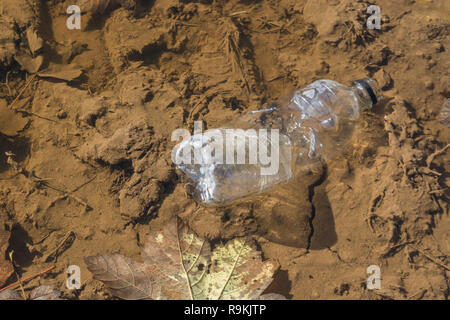 PTFE-Kunststoff Soft drink Flasche in schlammigen ländlichen Anschluss verworfen. Metapher Kunststoff Verschmutzung, Umweltverschmutzung, Krieg auf Kunststoffabfälle. Stockfoto