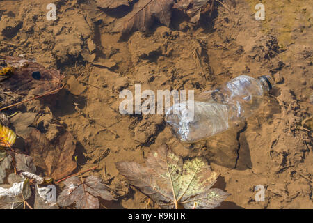 PTFE-Kunststoff Soft drink Flasche in schlammigen ländlichen Anschluss verworfen. Metapher Kunststoff Verschmutzung, Umweltverschmutzung, Krieg auf Kunststoffabfälle. Stockfoto