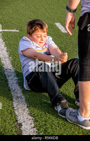 Als seine Mutter verbindlich seine Zehen hält, ein 8-jähriger Junge hat einige vorbereitende Sit Ups vor der Ausführung in einer Gemeinschaft Wettlauf im Costa Mesa, CA. Stockfoto