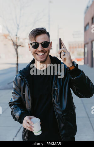Junge glücklich Tausendjährigen Mann Geschäftsmann Unternehmer in urbanen Innenstadt Metropole auf seinem Handy SMS und Unternehmen werden Anrufe, Kaffee Stockfoto