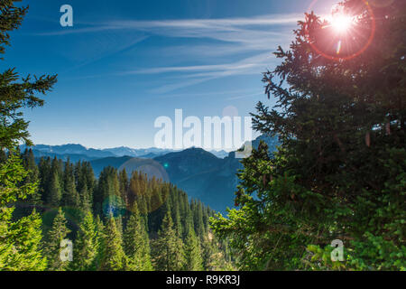 Blick gegen die Sonne über einem Tal am Tegelberg in Bayern auf die angrenzende Berglandschaft der Alpen in Richtung Österreich im Sommer mit Blau Stockfoto