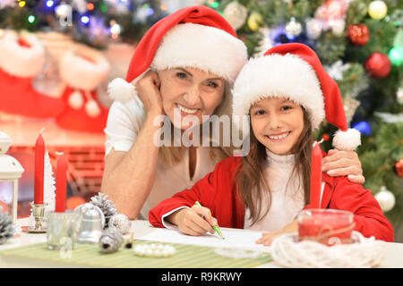Porträt der Großmutter mit Teen Girl in Santa Hüte Vorbereitungen für Weihnachten zu Hause Mädchen schreiben Stockfoto