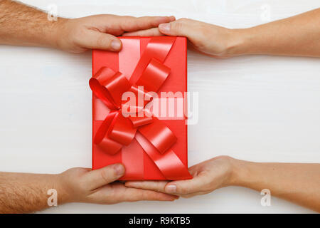 Nahaufnahme eines Menschen Hand ein rotes Kästchen mit einem Geschenk für eine Frau. Ansicht von oben. Konzept der Valentinstag und Weihnachtsfeier Stockfoto