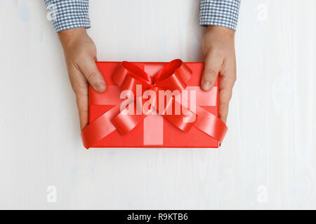 Nahaufnahme eines Menschen Hand geben ein rotes Kästchen mit einem Geschenk an den Tisch. Ansicht von oben. Konzept der Valentinstag und Weihnachtsfeier Stockfoto