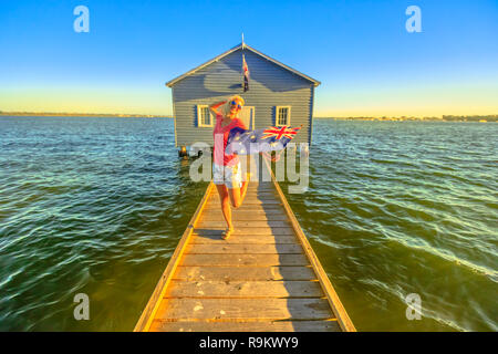 Happy kaukasische Frau mit australischen Flagge genießen vor blauen Boot Haus mit Holzsteg am Swan River bei Sonnenuntergang. Perth Sehenswürdigkeiten in Western Australia. Kopieren Sie Platz. Stockfoto